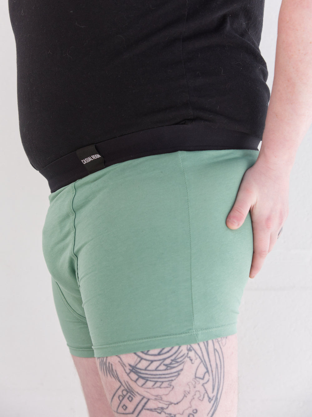 Model from the side, wearing green packing boxers and soft-form packer in front of a white background