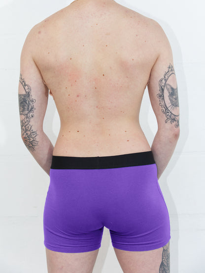 Person from behind, wearing purple packing boxer brief in front of a white background